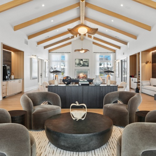 Clubroom with four grey chairs, a couch, coffee station, and fire place in distance
